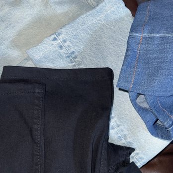 Hemmed jeans and dark trousers folded together after alterations at Brite Cleaners