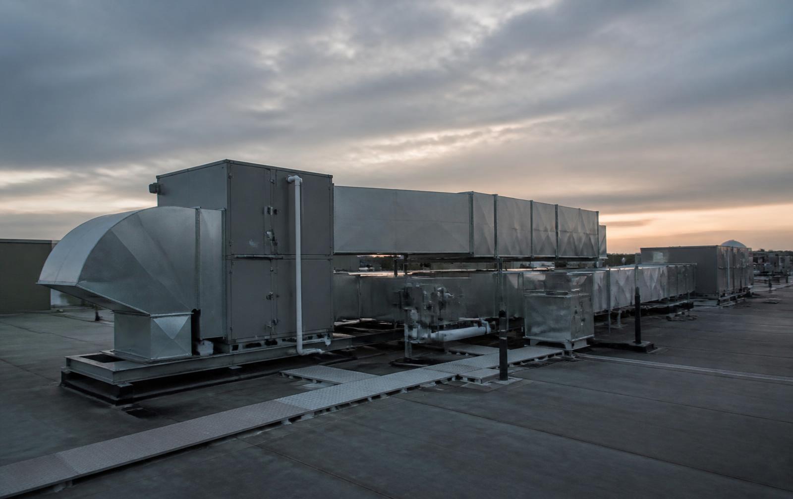 Rooftop air handling units and galvanized ductwork on a commercial building at dusk
