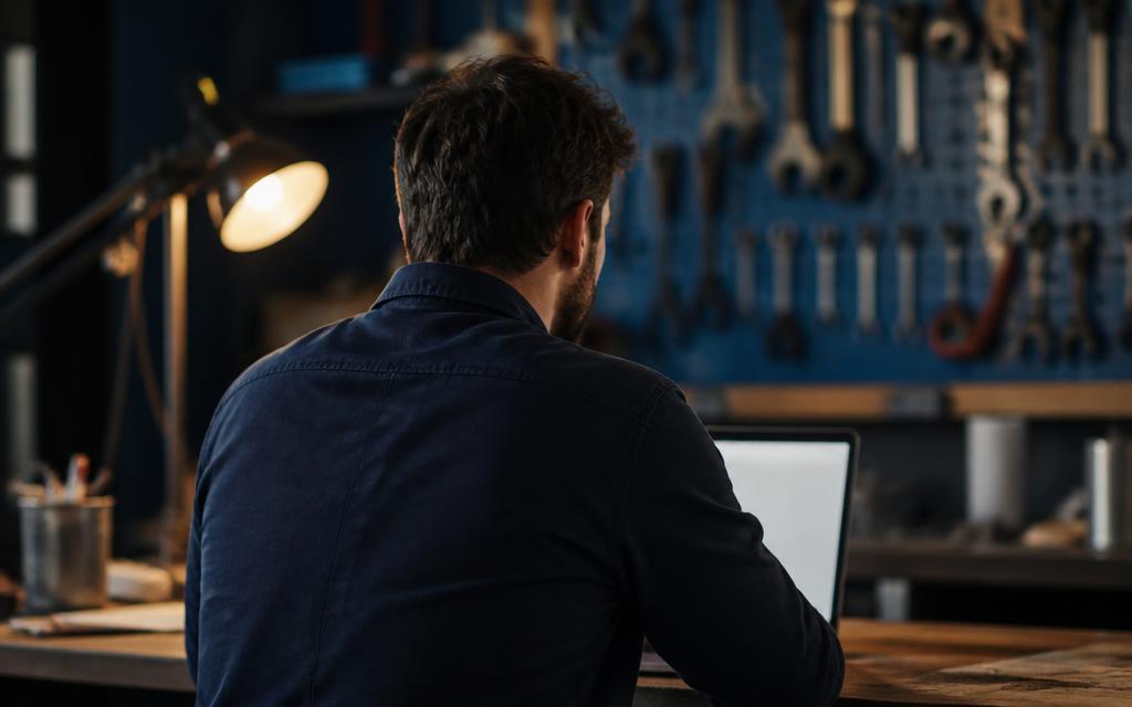 A business owner at a workbench desk reviewing his company's online presence on a laptop